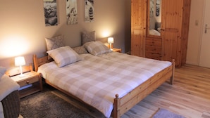 A bedroom with a wooden bed, two bedside tables with lamps, a wooden wardrobe, and wall art. - Cozy Apartment With Pool & Forest (Kirchdorf)