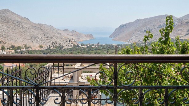 A balcony with wrought iron railings overlooking a coastal landscape with mountains and a body of water. - Pretty Holiday Home in Symi Island With Balcony (Symi)