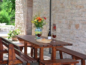 Un tavolo in legno all'aperto con un vaso di fiori, una bottiglia di vino e un bicchiere di vino.