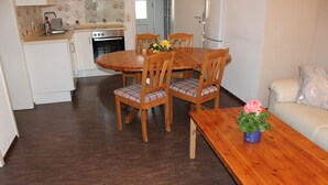 A compact kitchen with a dining table and chairs, a sofa, and a wooden coffee table with a flower vase. - Chicke Ferienwohnung in Struppen (Struppen)