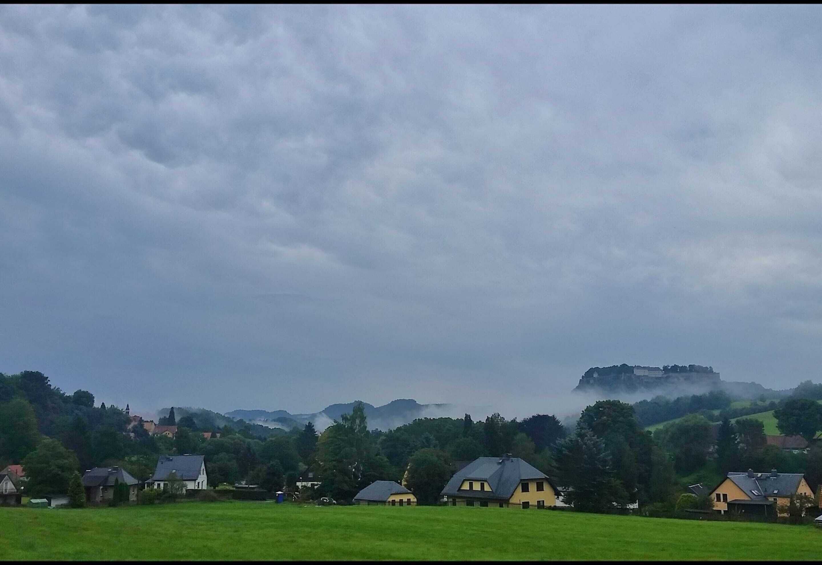 A rural landscape with houses, a hilltop castle, and a cloudy sky.