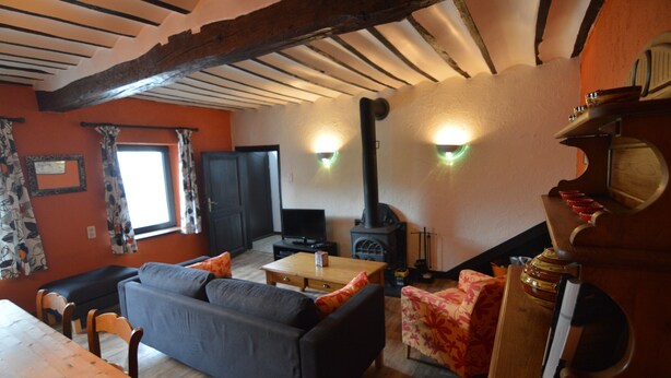 A cozy living room with a sofa, a wooden table, and a television. There is a fireplace and a window with curtains. - Holiday House in Horse Riding School near Stavelot & Spa Circuit (Stavelot)