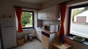 A compact kitchen with white cabinets, a microwave, a refrigerator, and a window with orange curtains. - Holiday House in Horse Riding School near Stavelot & Spa Circuit (Stavelot)
