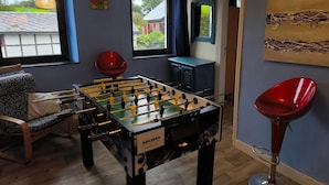 A room with a foosball table, a red chair, and a window with a view of houses. - Holiday House in Horse Riding School near Stavelot & Spa Circuit (Stavelot)