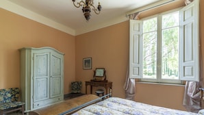 A bedroom with a bed, a wardrobe, a chair, a desk, and a window with curtains.