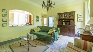 A living room with a green sofa, a glass coffee table, a chandelier, and a wooden cabinet with decorative items.