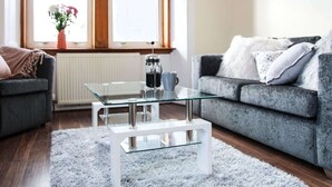 A modern living room with a glass coffee table, grey sofas, and a white rug.