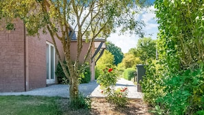 A brick building with a door and a small garden area with a tree and a flower bush. - Enticing Holiday Home in Treignes near Forest (Viroinval)