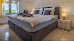 A modern bedroom with a large bed, a nightstand with a lamp, and a view of greenery through the window. - Graceful Apartment in Banjole near Beach Centinera (Medulin)
