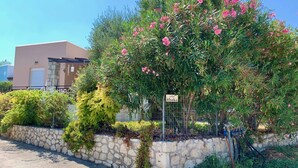 A villa named 'villa ithaka' with a stone wall, lush greenery, and pink flowering trees. - Beautiful, Modern, Luxuriously Villa, Private Swimming Pool 8 p NW Coast, Crete (Rethymno)