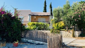 A two-story house with a stone facade, a balcony, and a garden with various plants and flowers. - Beautiful, Modern, Luxuriously Villa, Private Swimming Pool 8 p NW Coast, Crete (Rethymno)