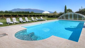 A swimming pool with a clear view of mountains in the background, surrounded by white lounge chairs and a glass-enclosed area. - Villa with Private Pool on an Estate near Assisi (Assisi)