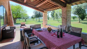 An outdoor patio with wicker furniture, a checkered tablecloth, and a view of a grassy landscape. - Villa with Private Pool on an Estate near Assisi (Assisi)