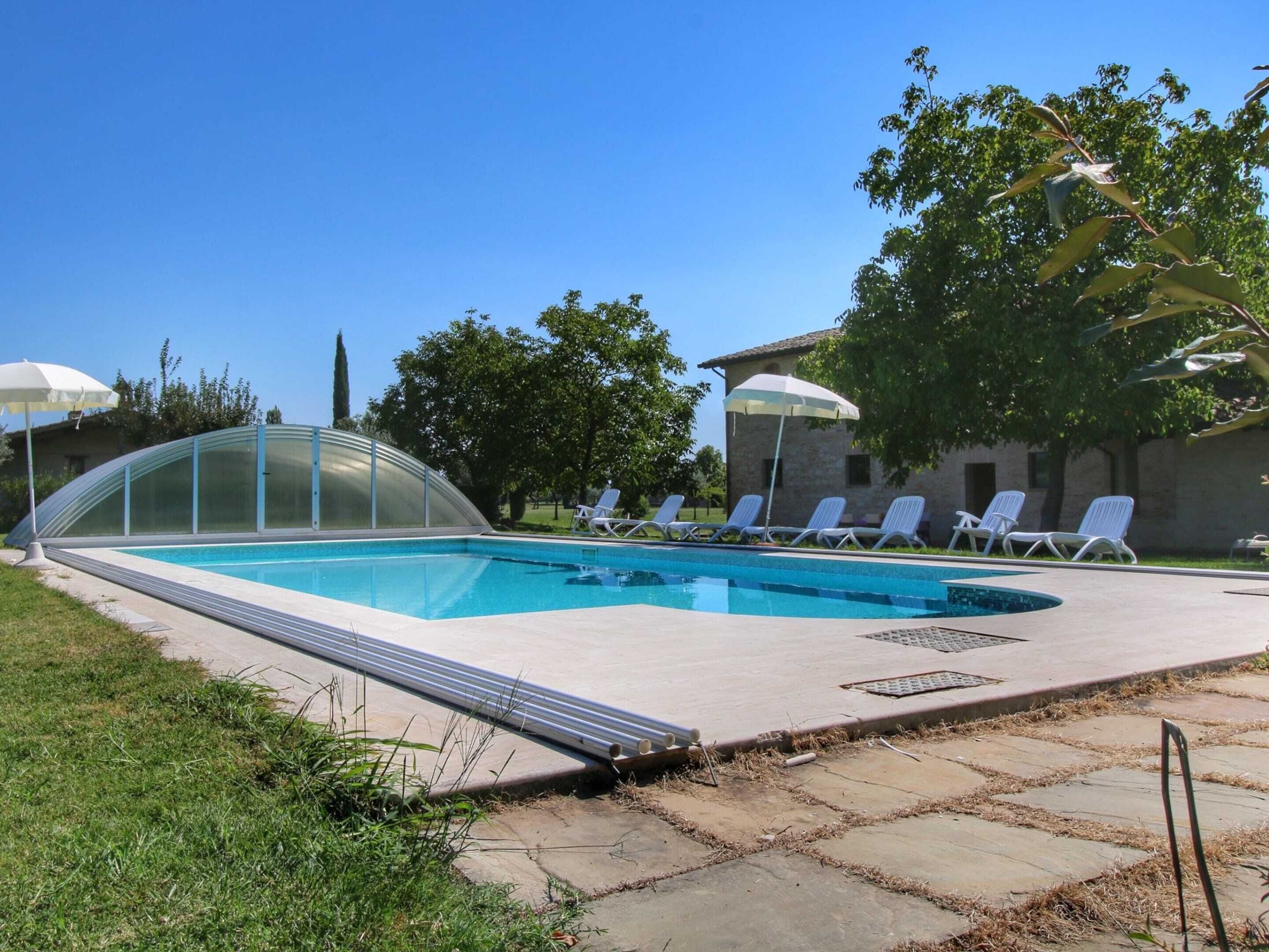 A swimming pool with a glass enclosure, surrounded by lounge chairs and umbrellas.