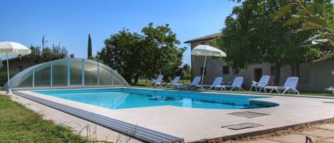 A swimming pool with a glass enclosure, surrounded by lounge chairs and umbrellas.
