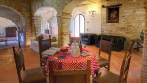 A dining area with a red and white checkered tablecloth, leather chairs, and a stone wall with arched doorways. - Villa with Private Pool on an Estate near Assisi (Assisi)