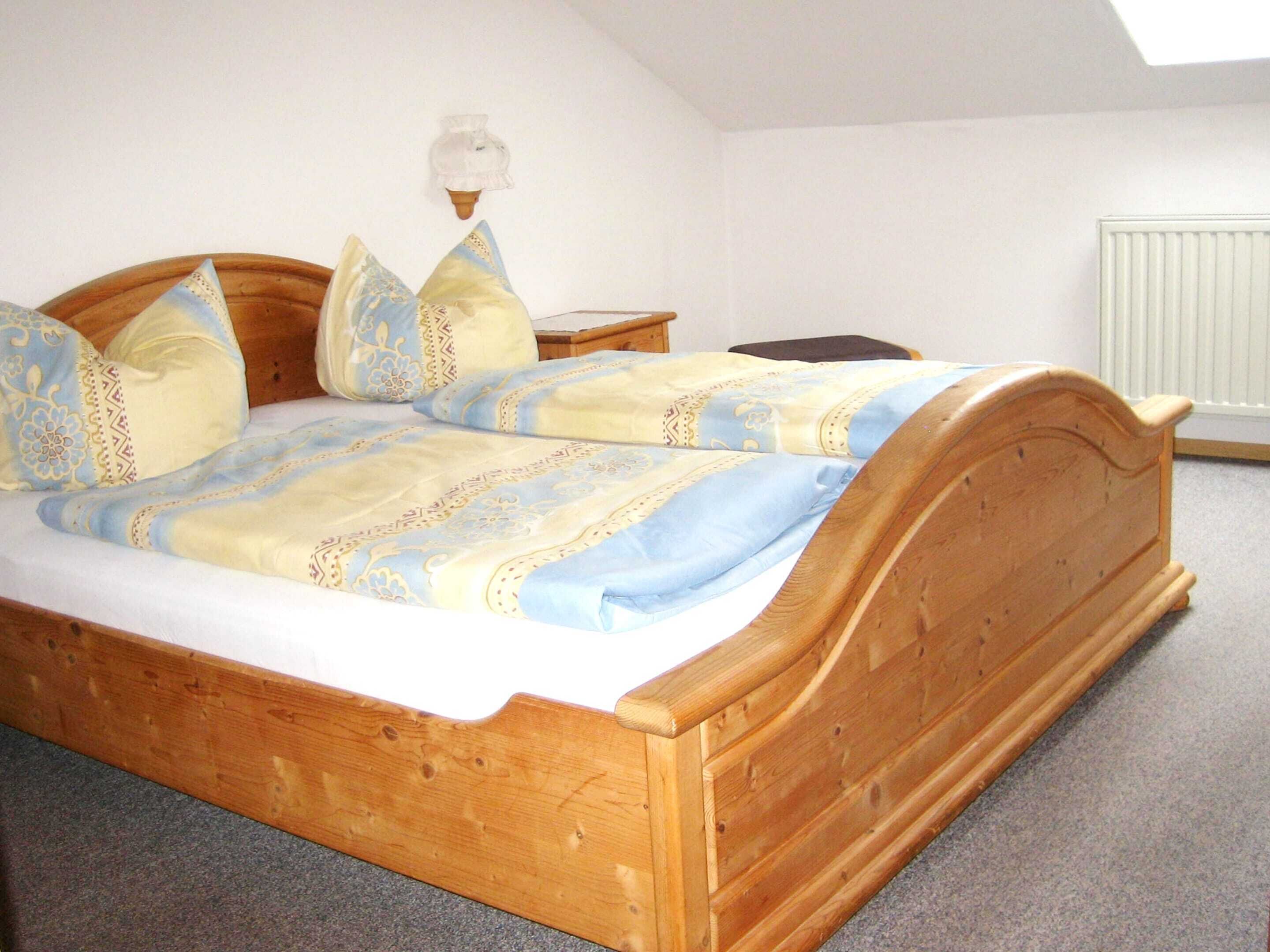 A wooden bed with a patterned bedspread, a bedside table, and a wall-mounted light fixture.