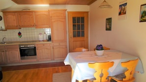 A kitchen with wooden cabinets, a stove, and a dining area with a table and chairs. - Apartment in Ingenried With Bavarian Alps View (Ingenried)
