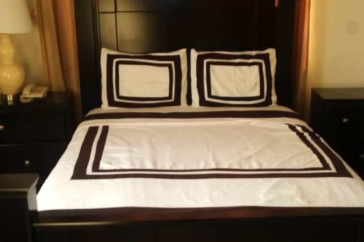 A bed with a black frame, white bedding with black trim, and a red rug on the floor.