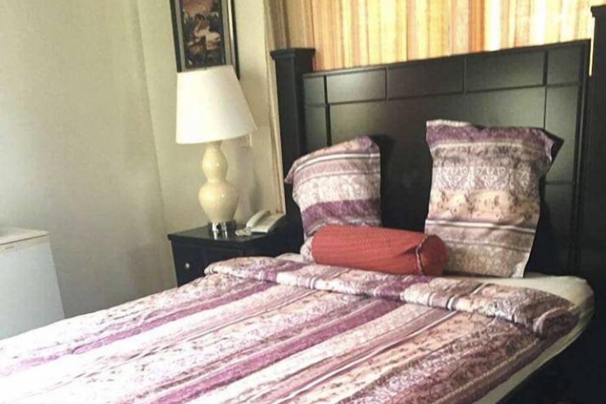 A bed with a patterned bedspread, a nightstand with a lamp, and a wall-mounted picture.