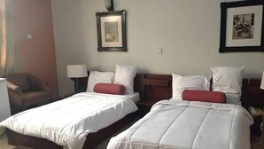 Quarto de hotel com duas camas, uma cadeira, um abajur e quadros na parede.