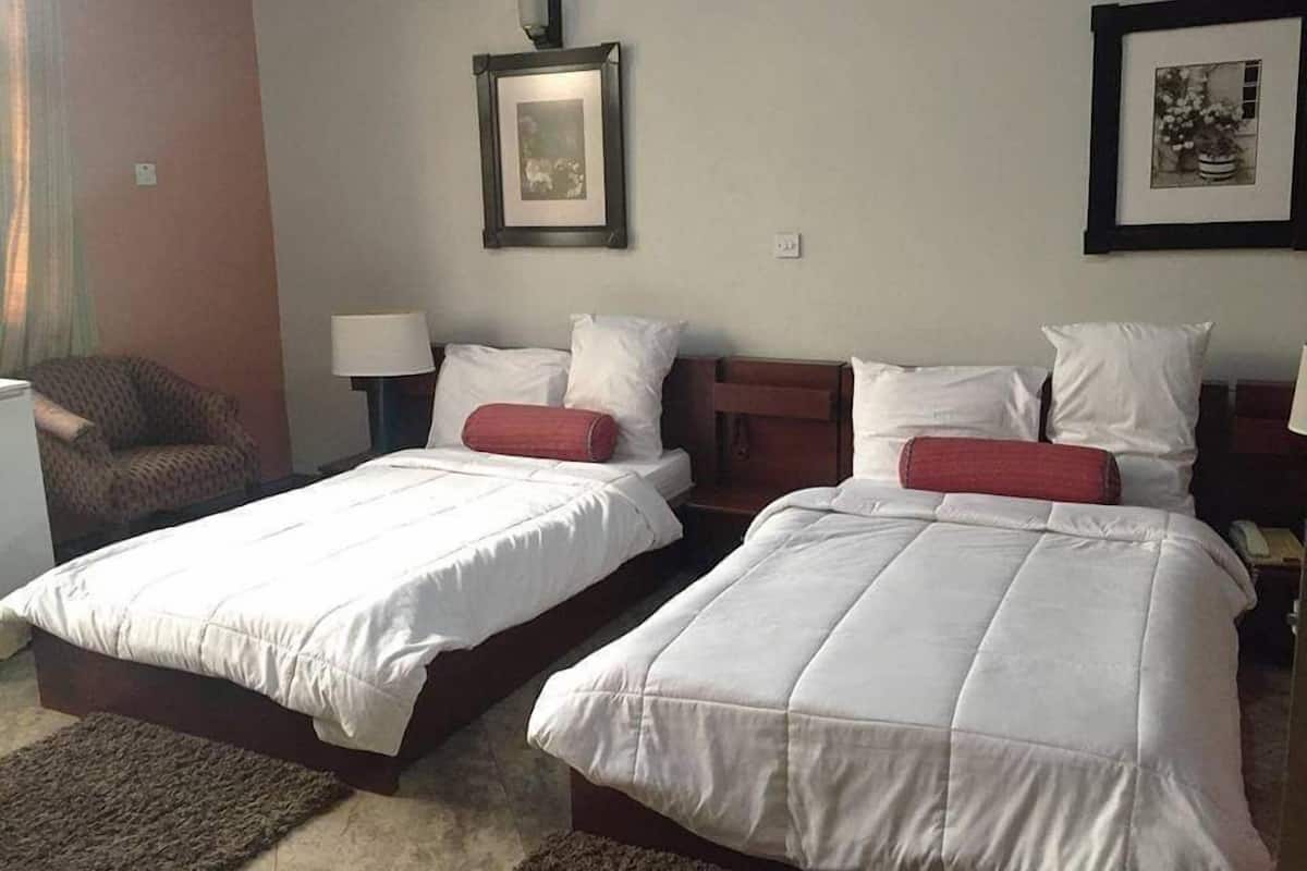 A hotel room with two beds, a chair, a lamp, and framed pictures on the wall.