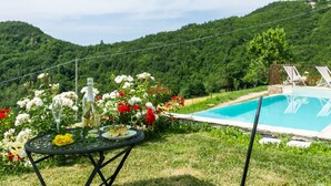 Un cadre agréable au bord de la piscine, avec une table, des fleurs et une vue sur un paysage montagneux.