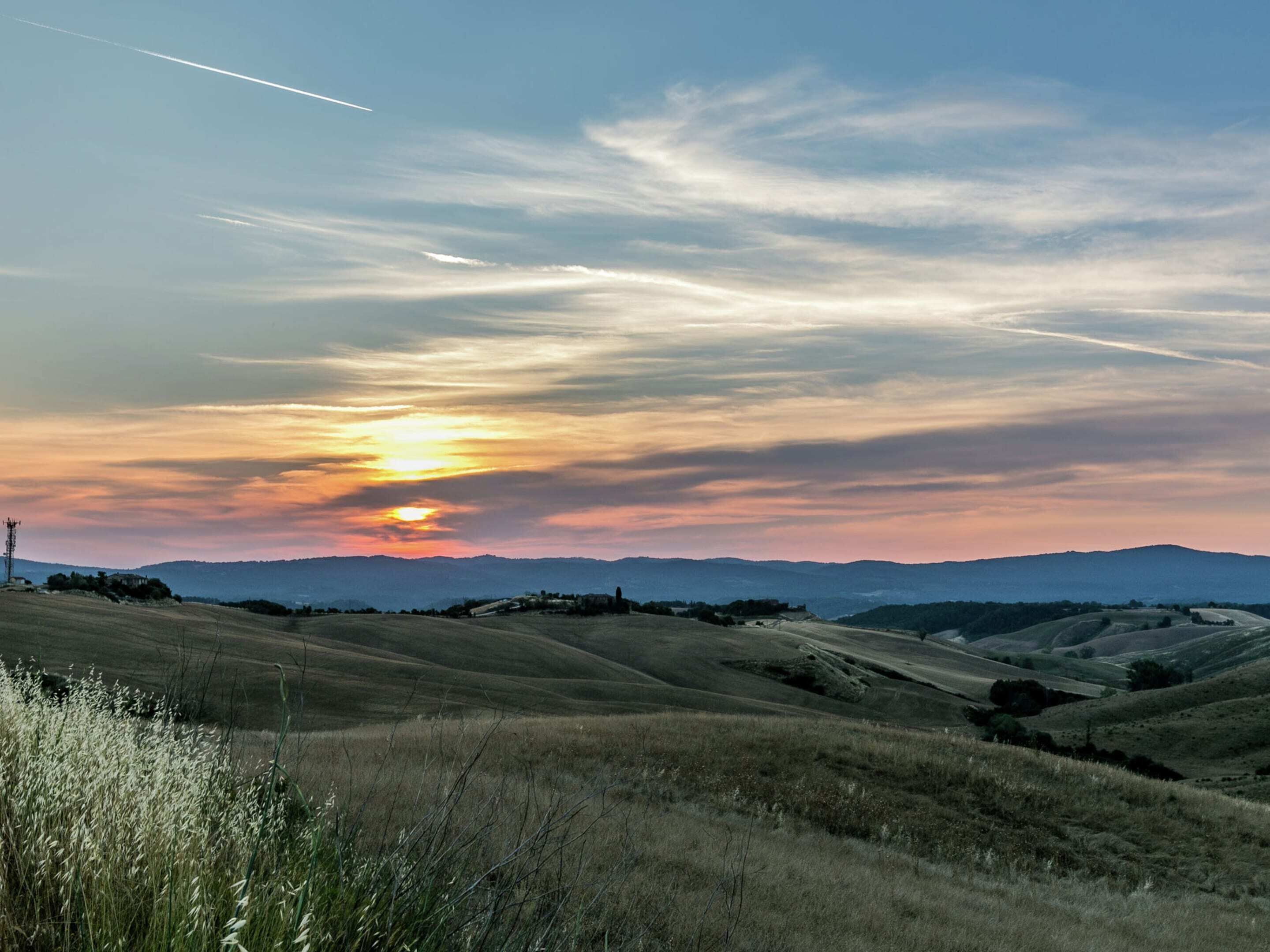 Ein Sonnenuntergang über sanften Hügeln, mit blauem Himmel und fernen Bergen.