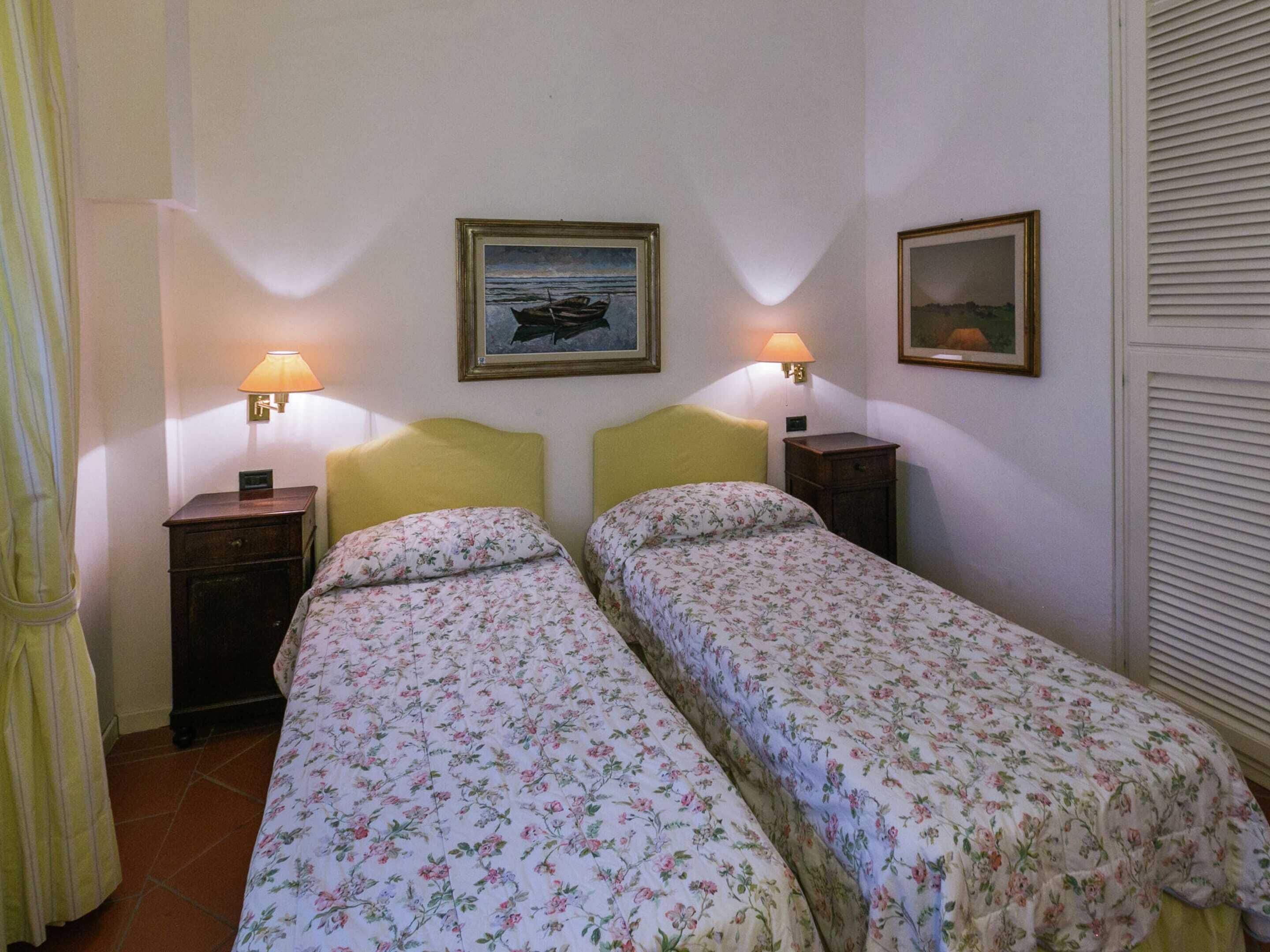 Ein Zimmer mit zwei Betten, jeweils mit floralem Bettbezug und Kopfteil. Zwei Wandlampen, ein gerahmtes Bild eines Bootes und ein gerahmtes Landschaftsbild sind vorhanden.