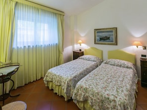 A room with two beds, a chair, a table, and a painting on the wall.
