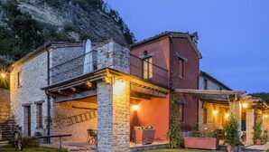 A stone house with a balcony and a red-roofed extension, surrounded by a garden and a hillside. - Belvilla by Oyo Il Vettore nei Monti Sibillini (Monte San Martino)