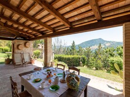 A covered outdoor dining area with a table set for breakfast, overlooking a scenic landscape.