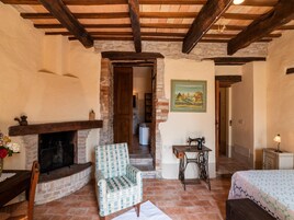 A rustic room with exposed wooden beams, a fireplace, a vintage sewing machine, and a cozy chair.