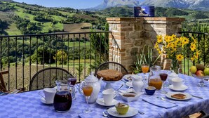 Una mesa lista para el desayuno con vistas a la montaña, un muro de piedra y un jarrón de flores.