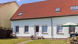 Een tweelaags huis met een rode pannendak, witte buitenmuren en een klein voortuintje met een bankje.
