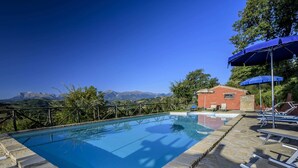 Ein Pool mit Steinfliesen, Liegestühlen und Blick auf Berge.