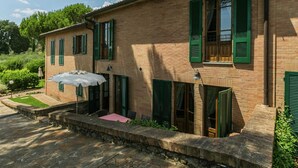 Una casa a due piani in mattoni con persiane verdi, un vialetto in pietra e un patio con tavolo e sedie.