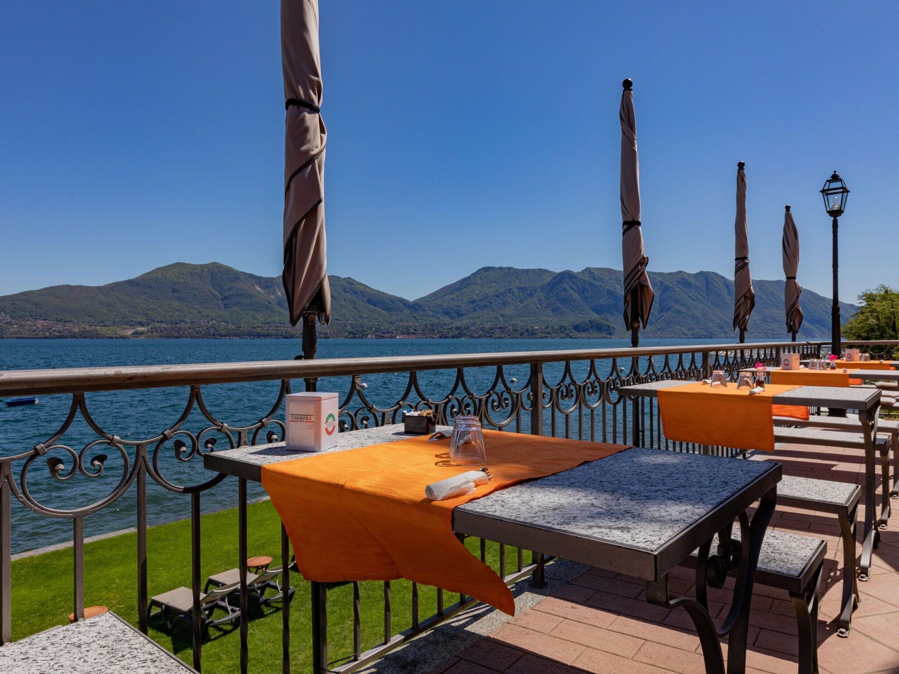 An outdoor terrace with tables and chairs, overlooking a lake and mountains.