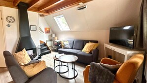 Een gezellige woonkamer met een open haard, bank, fauteuil en televisie.