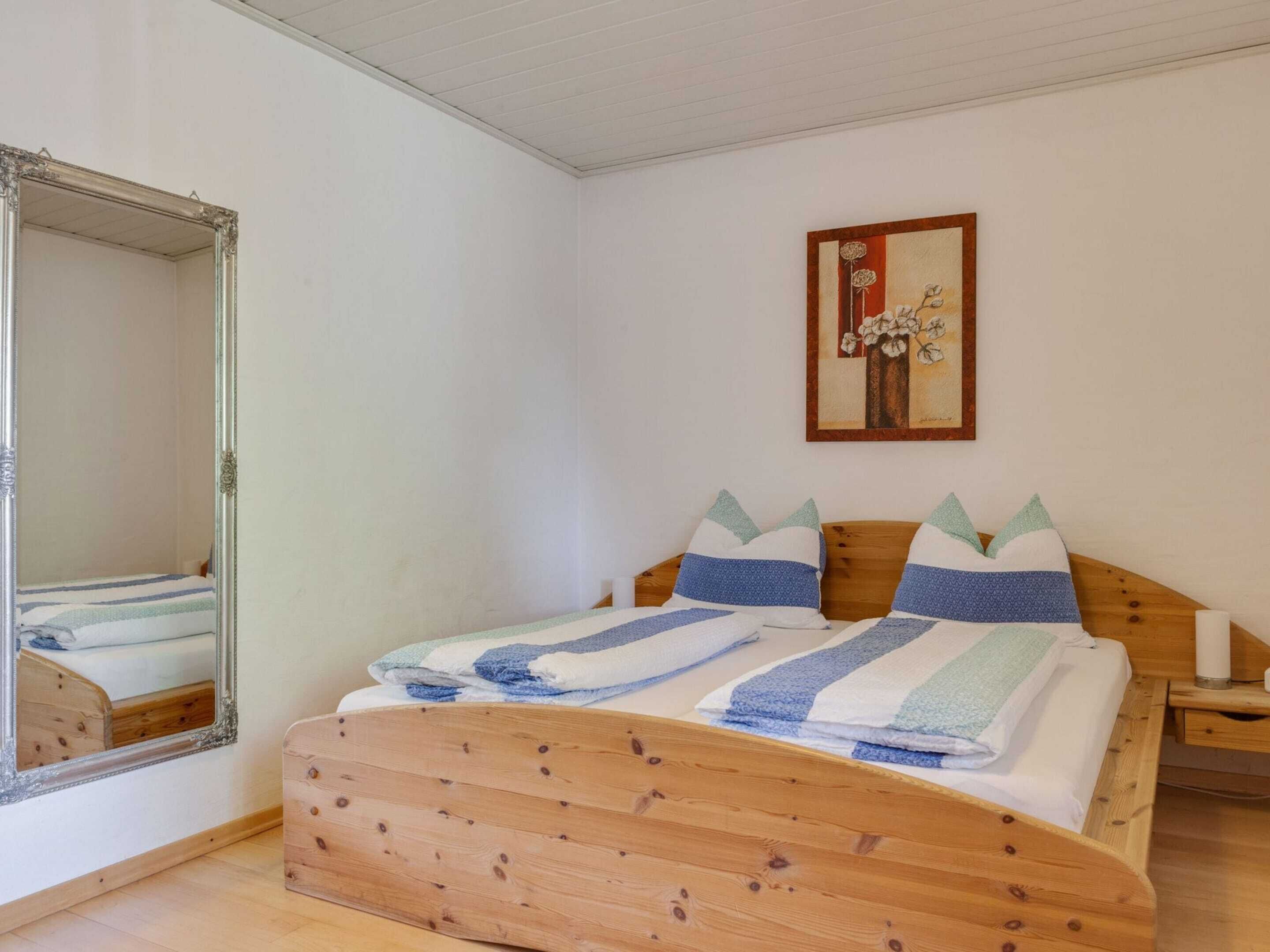 Een slaapkamer met een houten bed, een grote spiegel en een kunstwerk in een lijst aan de muur.
