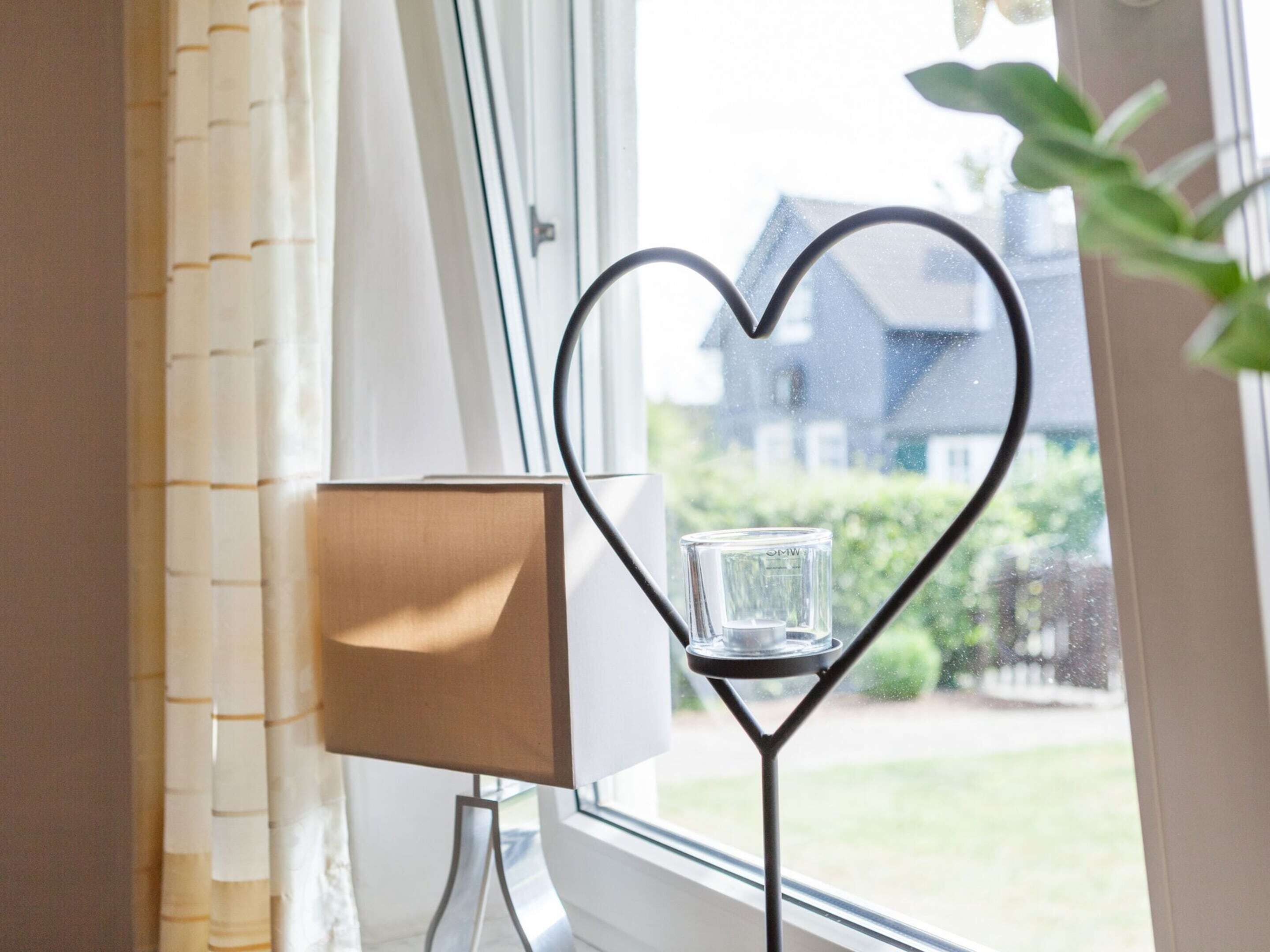 Une pièce avec une fenêtre, un porte-bougie en forme de cœur avec une bougie, et une lampe sur un pied.