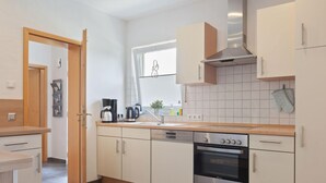 A modern kitchen with white cabinets, a stainless steel oven, a coffee maker, and a window with blinds. - Entspannender Ruckzugsort in Langewiese (Winterberg)
