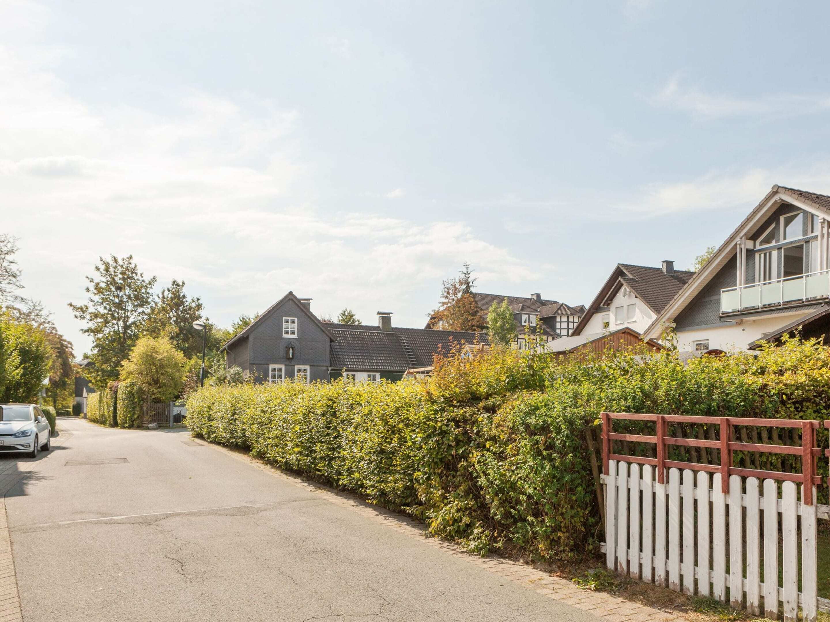 Eine Wohnstraße mit Häusern, einem weißen Zaun und einem geparkten Auto.