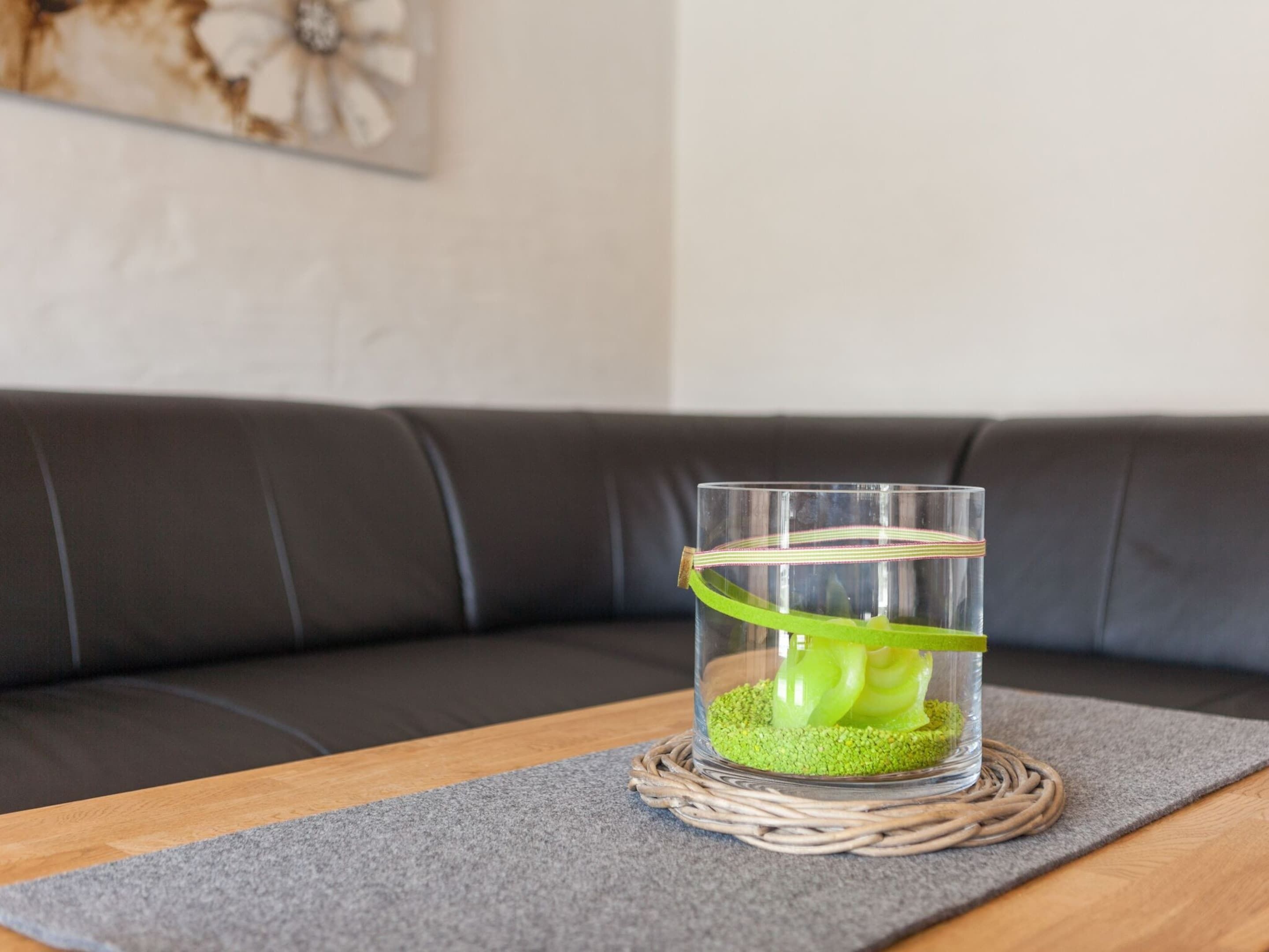 A clear glass vase with a green ribbon on a woven coaster, placed on a grey mat on a wooden table.