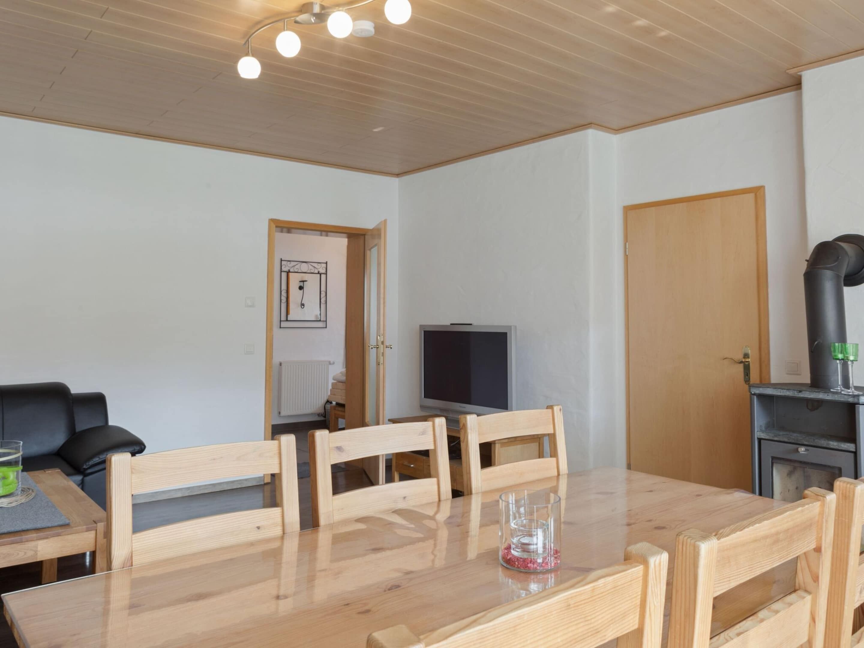 A room with a wooden dining table, four chairs, a television, a fireplace, and a door.