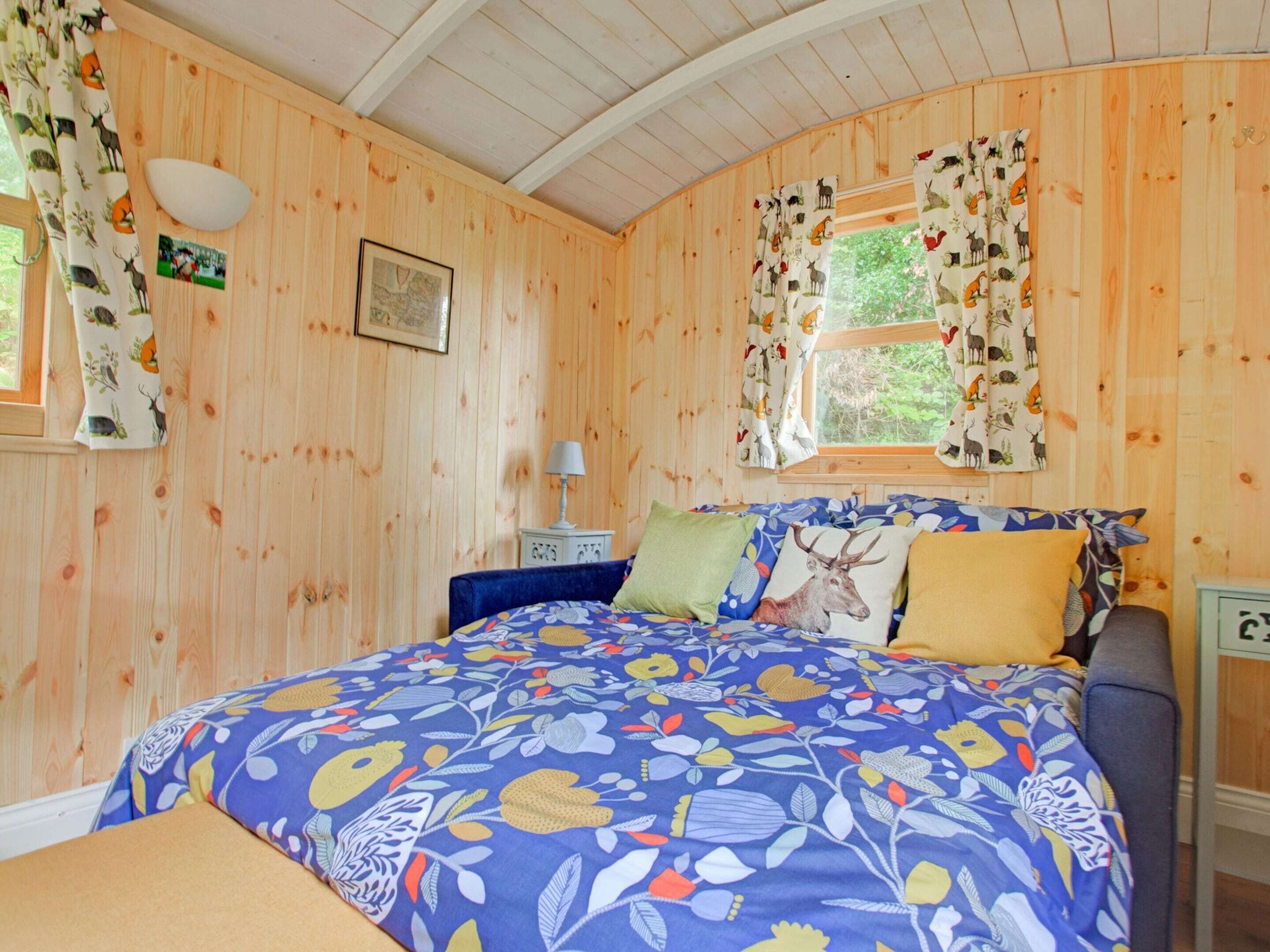 A wooden room with a bed, a nightstand, a lamp, and a window with curtains.