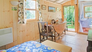 A cozy wooden room with a bed, a table with chairs, and a window with curtains.