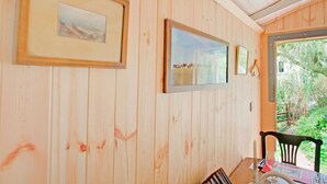 A wooden-paneled room with framed pictures on the wall, a table with a candle, and a view of greenery outside.