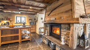 Eine rustikale Küche mit Kamin aus Stein, Holzbalken und Fliesenboden.