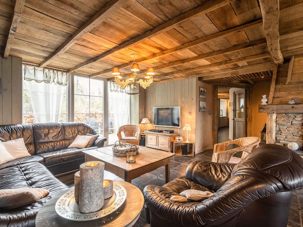A cozy living room with leather sofas, a stone fireplace, and a wooden ceiling.